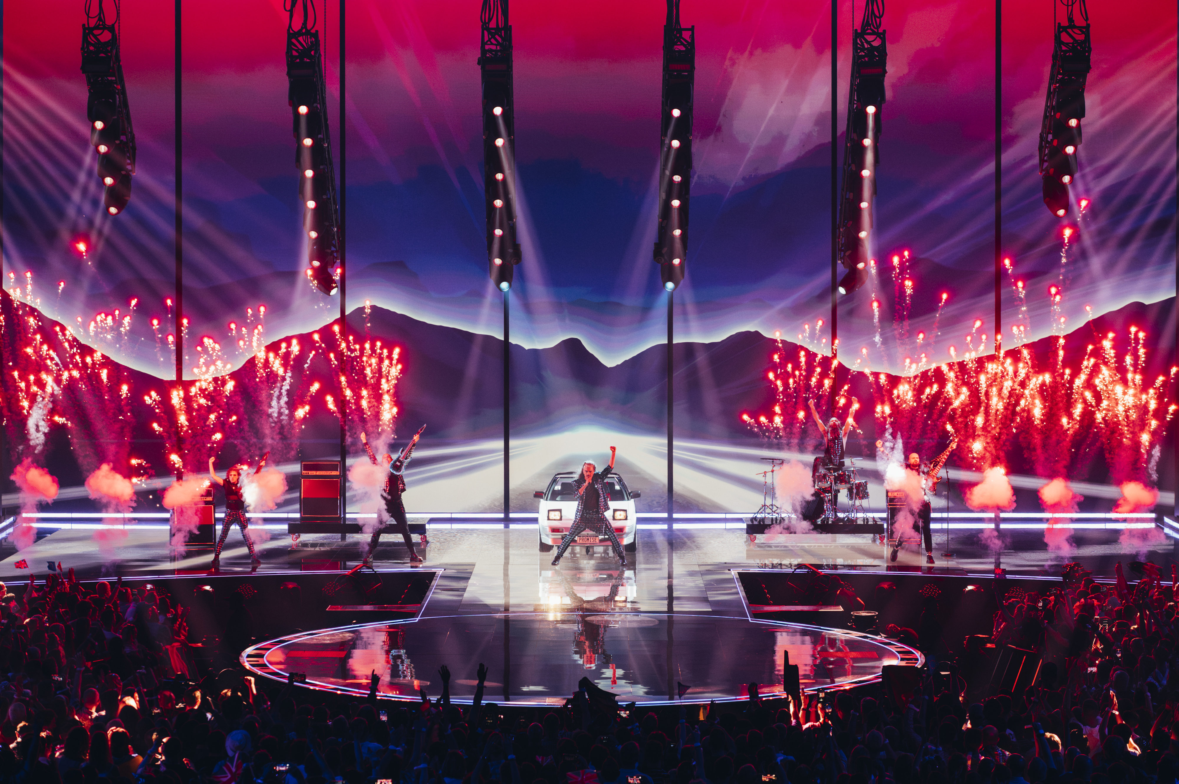 Voyager on stage for Australia at the Eurovision 2023 grand final. The band are on stage accompanied by an old white car and are performing with pyrotechnics going off in the background