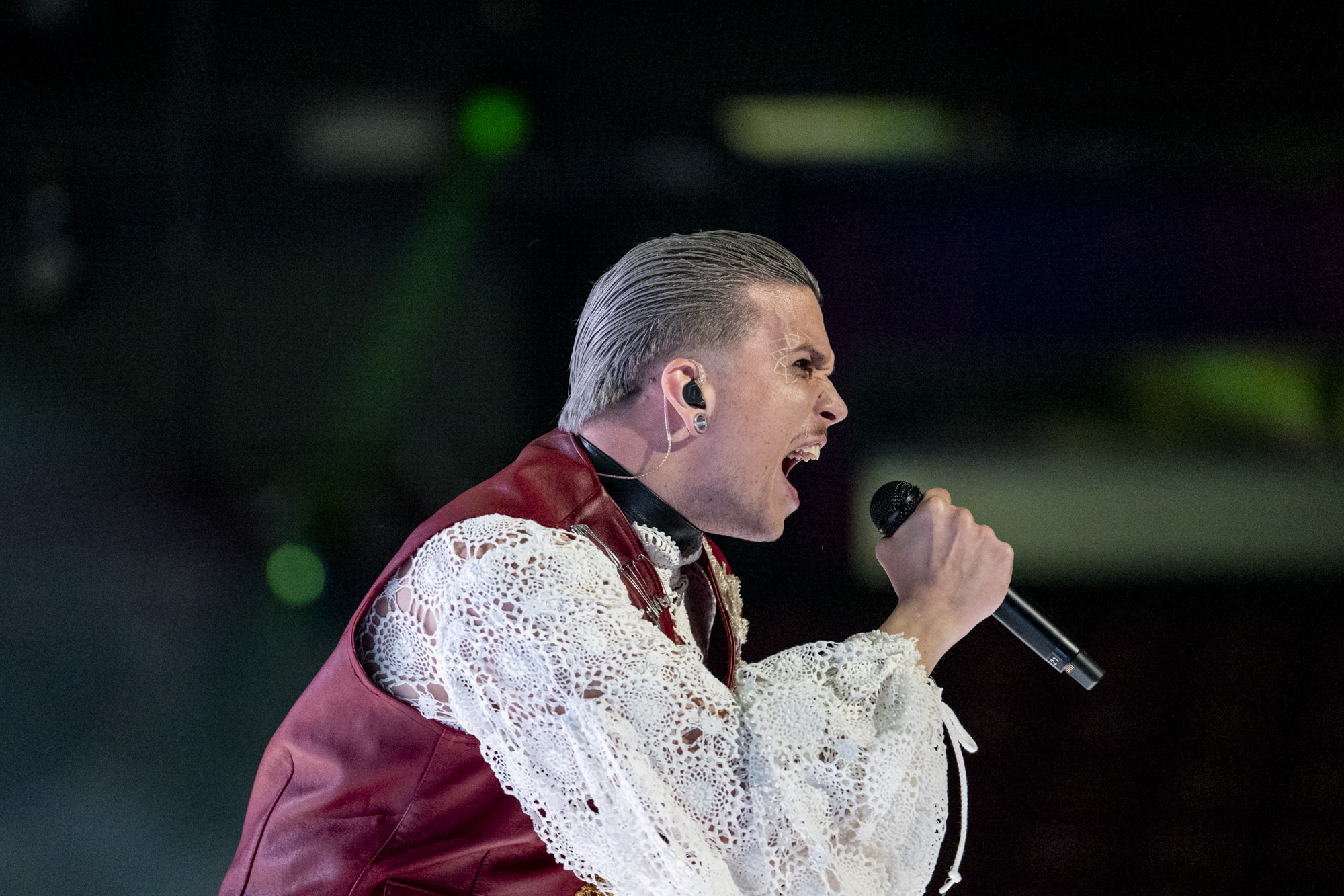 Baby Lasagna during the first rehearsal. He is loudly singing in the microphone, dressed in a frilly white shirt and a dark red chest piece.