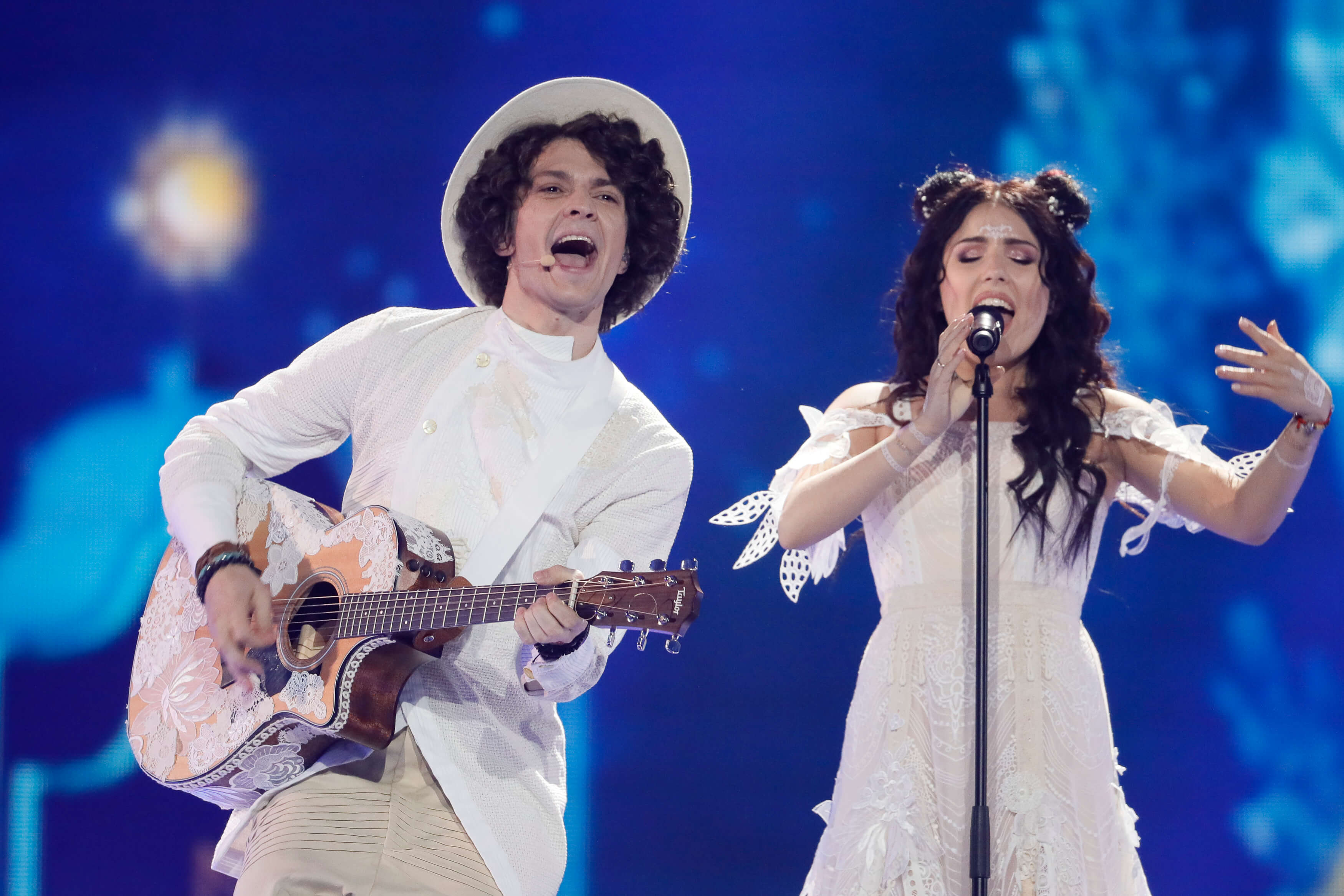 NAVIBAND performing at the Eurovision Song Contest. Ksenija is singing into the microphone stand while Artsiom stands next to her singing and playing the guitar.